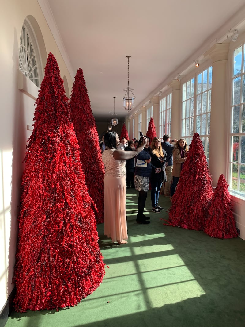 A woman taking a selfie in front of conical red Christmas trees on a green carpet
